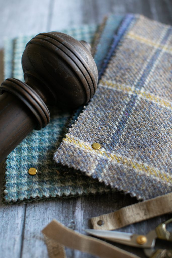 A wooden curtain pole and some wool fabric samples, a pair of scissors and a fabric tape measure on a wooden table.