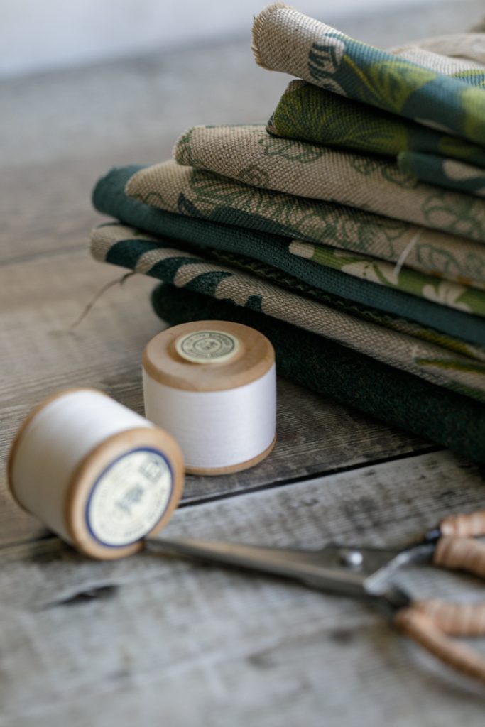 A neatly folded pile of blue and green linens with a pair of scissors and cotton reels next to them