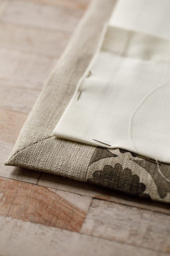 A roman blind being hand sewn with a cream lining, and a needle and thread and pins