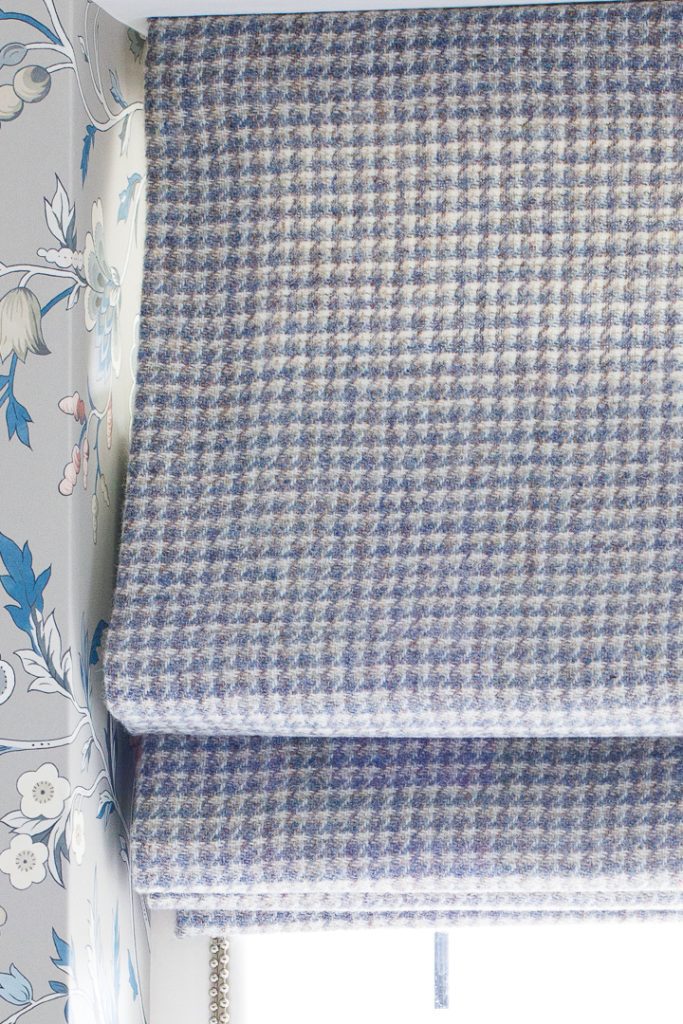 A window with a wool houndstooth blue and white check roman blind and a blue patterned wallpaper around the recess